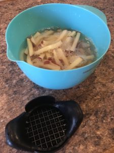 Potatoes cut into french fries and soaking in water to remove starch
