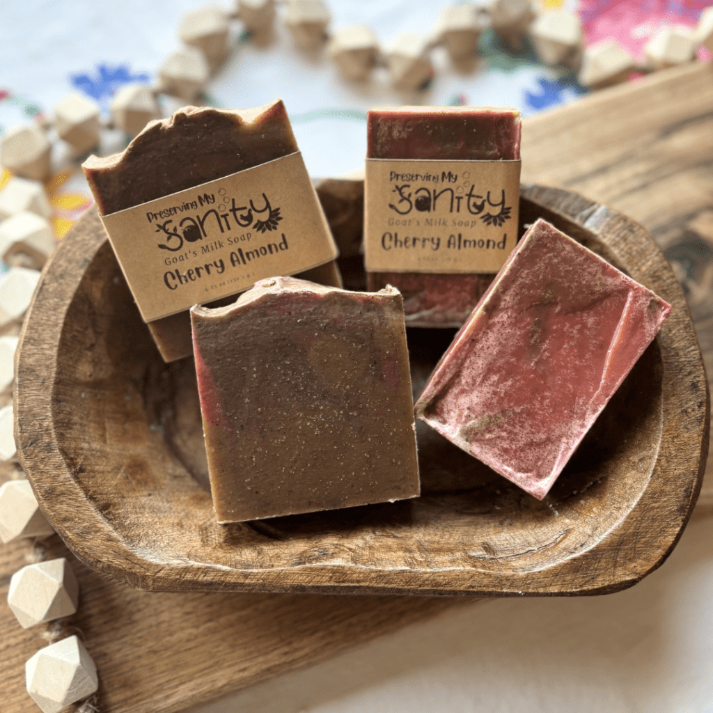 Flatlay photo showing four bars of Cherry Almond goat's milk soap in a wooden bowl, two bars of each size that are available in the shop.