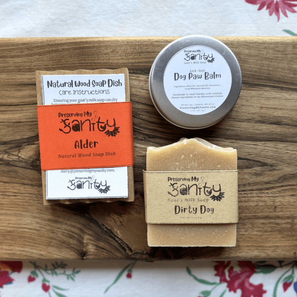 Flatlay photo of Dirty Dog goat's milk soap, dog paw balm, and a natural wood soap dish