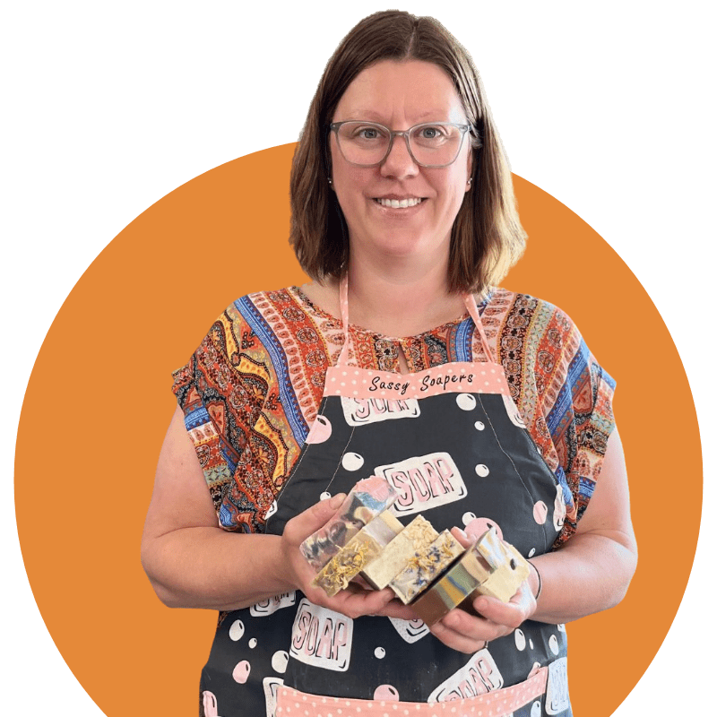Photo of Darcy, soapmaker and Preserving My Sanity owner, holding some bars of her handmade goat's milk soap and wearing a soap apron
