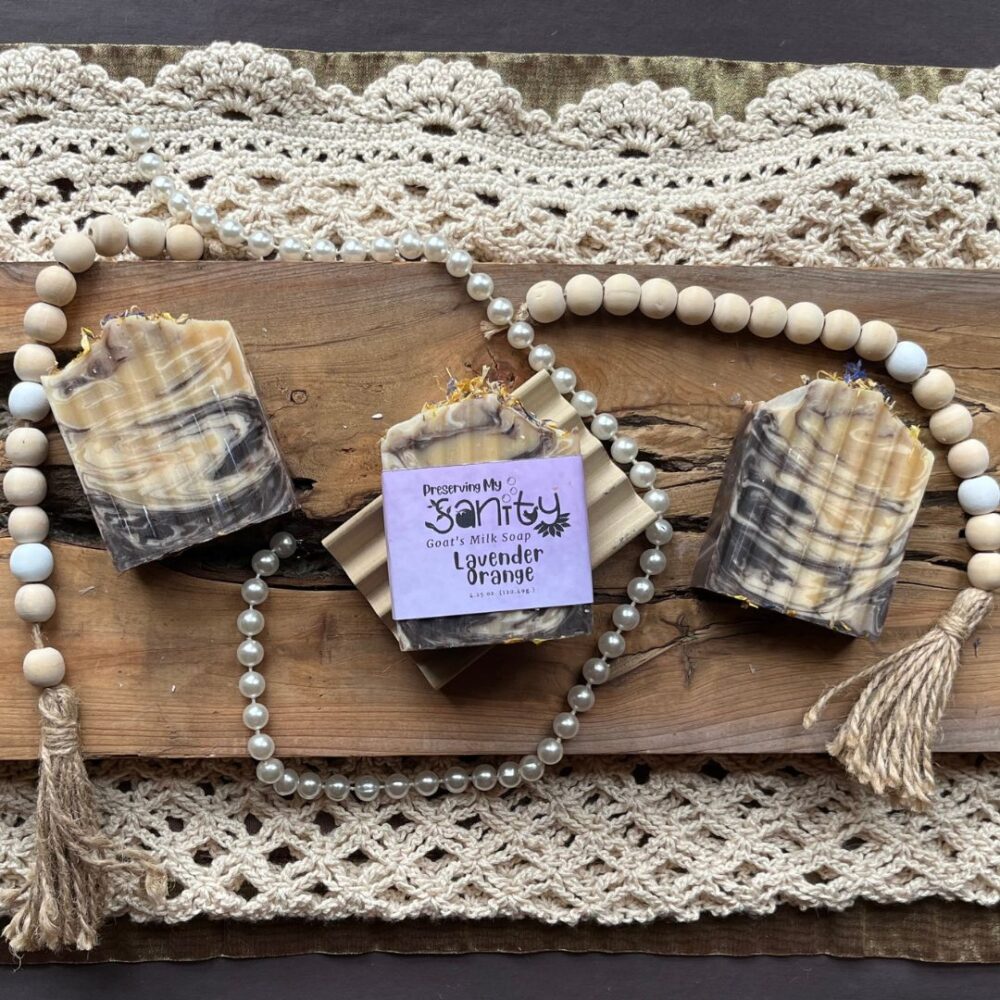 Pretty interior flatlay of bars of lavender orange soap with a backdrop of rustic wood, crochet, pearls, and wooden beads