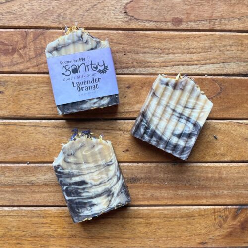 Plain flatlay of three bars of lavender orange soap with a stained wood background