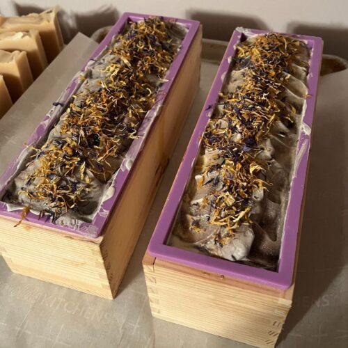 Interior photo of bars of lavender orange soap in the molds prior to cutting, with colorful flowers on top