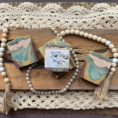 Pretty interior flatlay of mountain sky soap on a background of rustic wood, crochet, wooden beads, and pearls