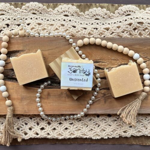Pretty interior flatlay of bars of unscented goat's milk soap with a made in the usa wooden soap holder, on a backdrop of rustic wood, pearls, wooden beads, and crochet