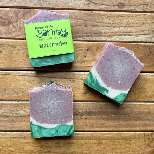 Plain interior flatlay of three bars of watermelon soap on a stained wood table background