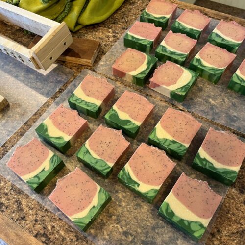 Interior flatlay photo of bars of watermelon soap just after cutting. They look just like watermelon with a green outer rind, white inner rind, and pink inside with poppy seeds.