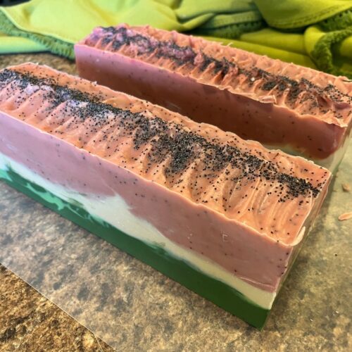 Side view of two loaves of watermelon soap before cutting, with green tablecloth in the background