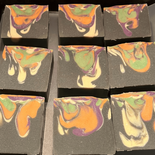 Flatlay photo of several bars of Fright Night Halloween-themed soap, black with drop swirl of orange, green, white, and purple.