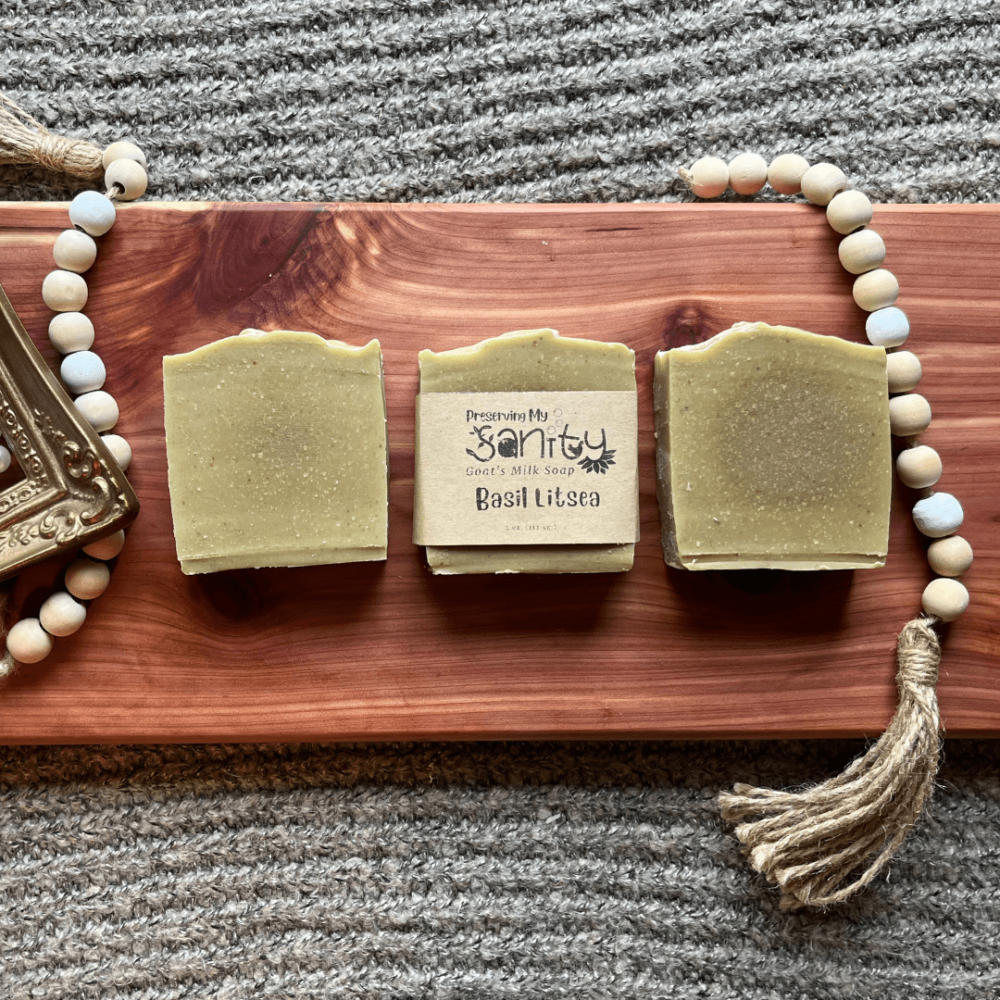 Flatlay photo of three bars of Basil Litsea infused and essential oil goat's milk soap on a handcrafted cedar bath board