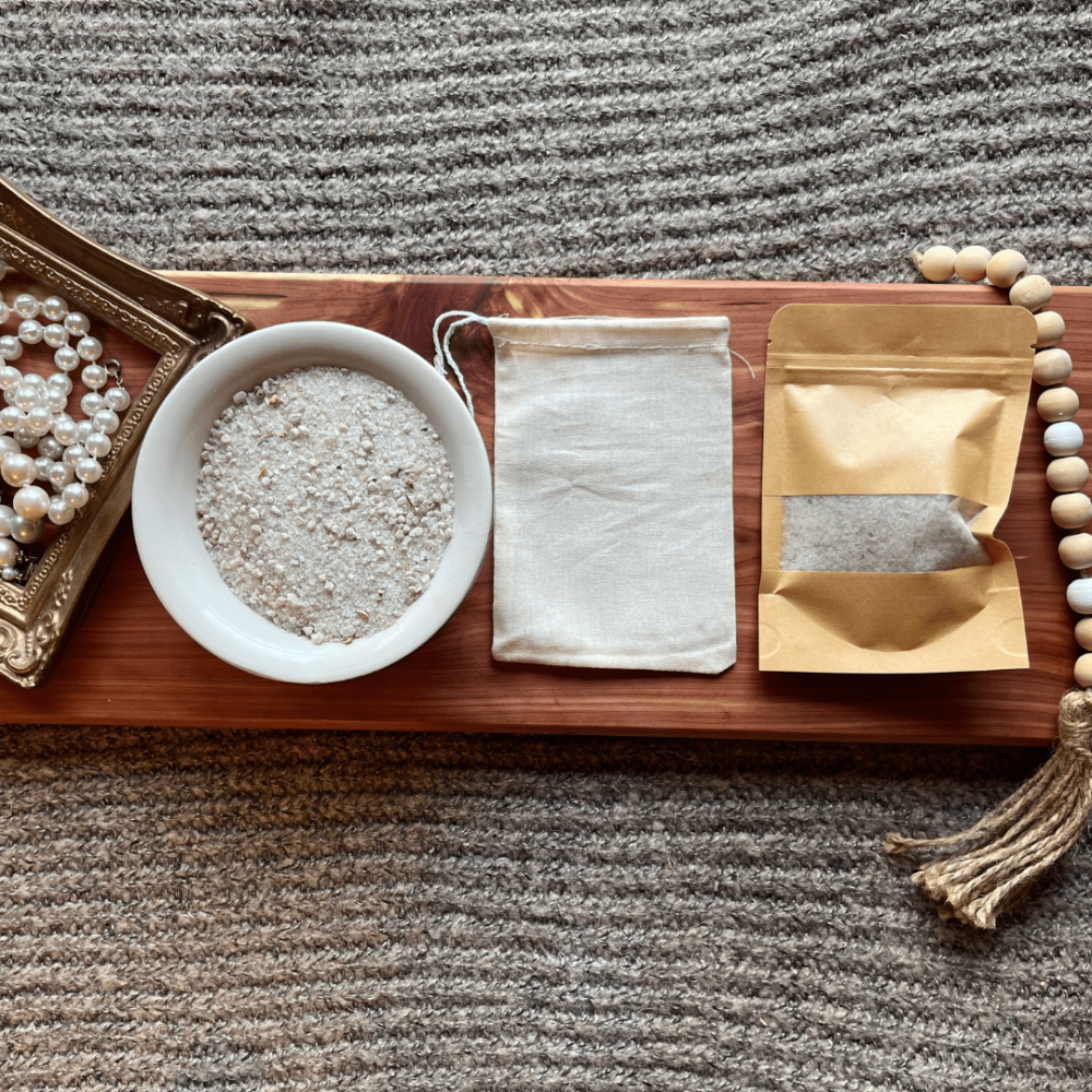 Flatlay photo showing a bowl of chamomile bath salt, with a package of bath salt and a reusable cheesecloth bag.