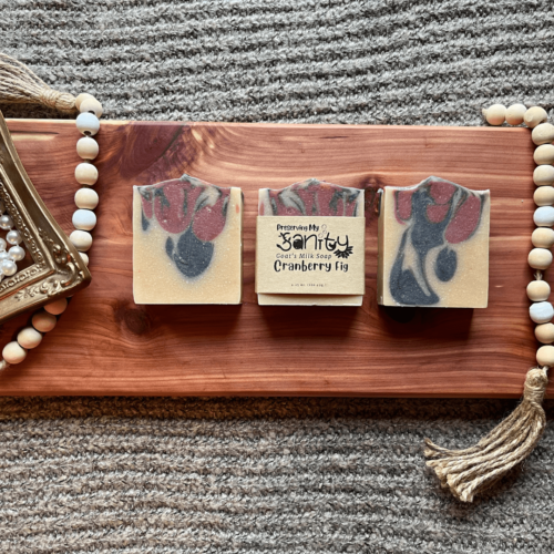 Flatlay photo showing three bars of cranberry fig goat's milk soap on a cedar bath board