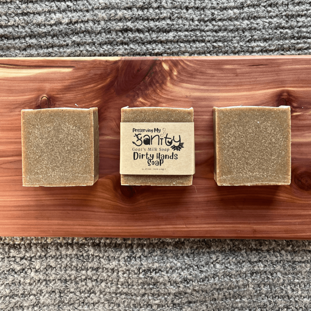Flatlay photo of three bars of Dirty Hands Soap on a cedar board with gray sweater backdrop