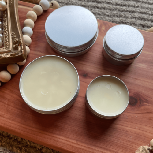 Alternate view flatlay photo of 1 ounce and 2 ounce tins of lick-safe dog paw balm on a cedar board