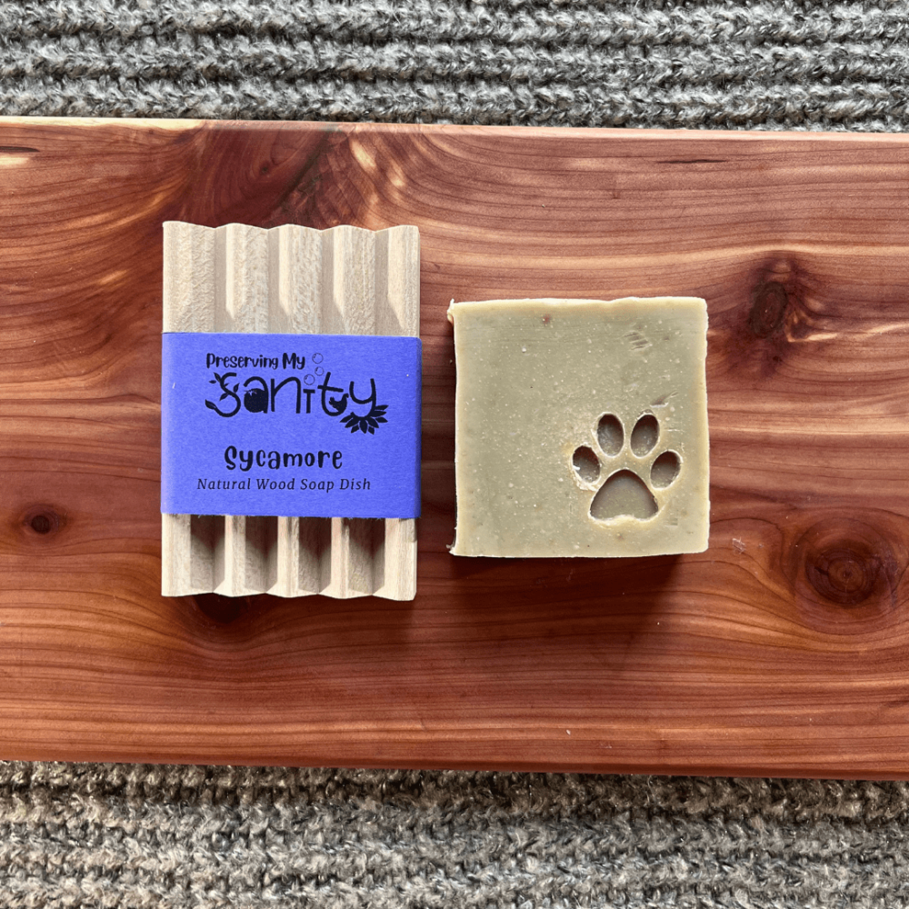 Flatlay photo of a bar of dog soap with a natural wood soap dish on a cedar board with a gray sweater backdrop