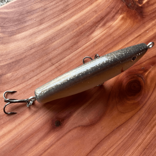Flatlay photo of a handmade Marshall's Minnows fishing lure in Black Shad color, showcasing top view with sun reflecting on back.