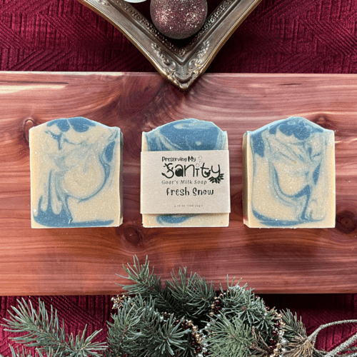 Three bars of Fresh Snow holiday soap on a cedar board in a holiday-themed flatlay.