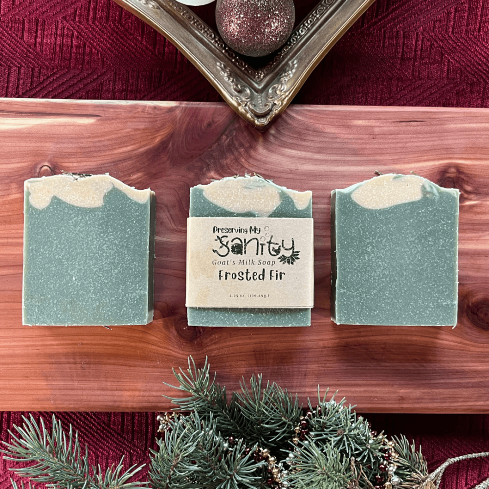 Three bars of Frosted Fir goat's milk soap on a cedar board among a holiday-themed flatlay