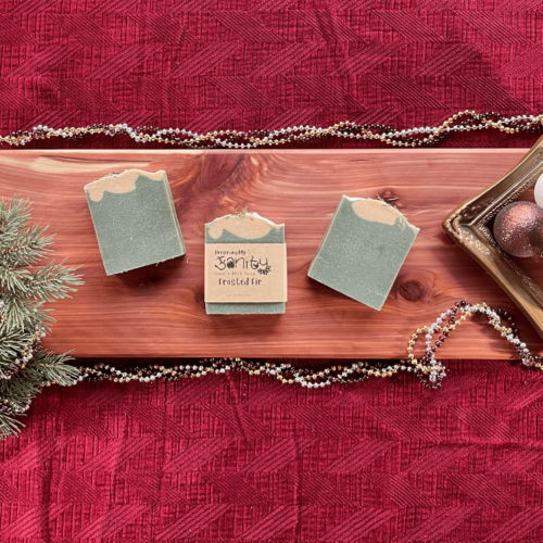 Holiday-themed flatlay of three bars of Frosted Fir goat's milk soap on a cedar board