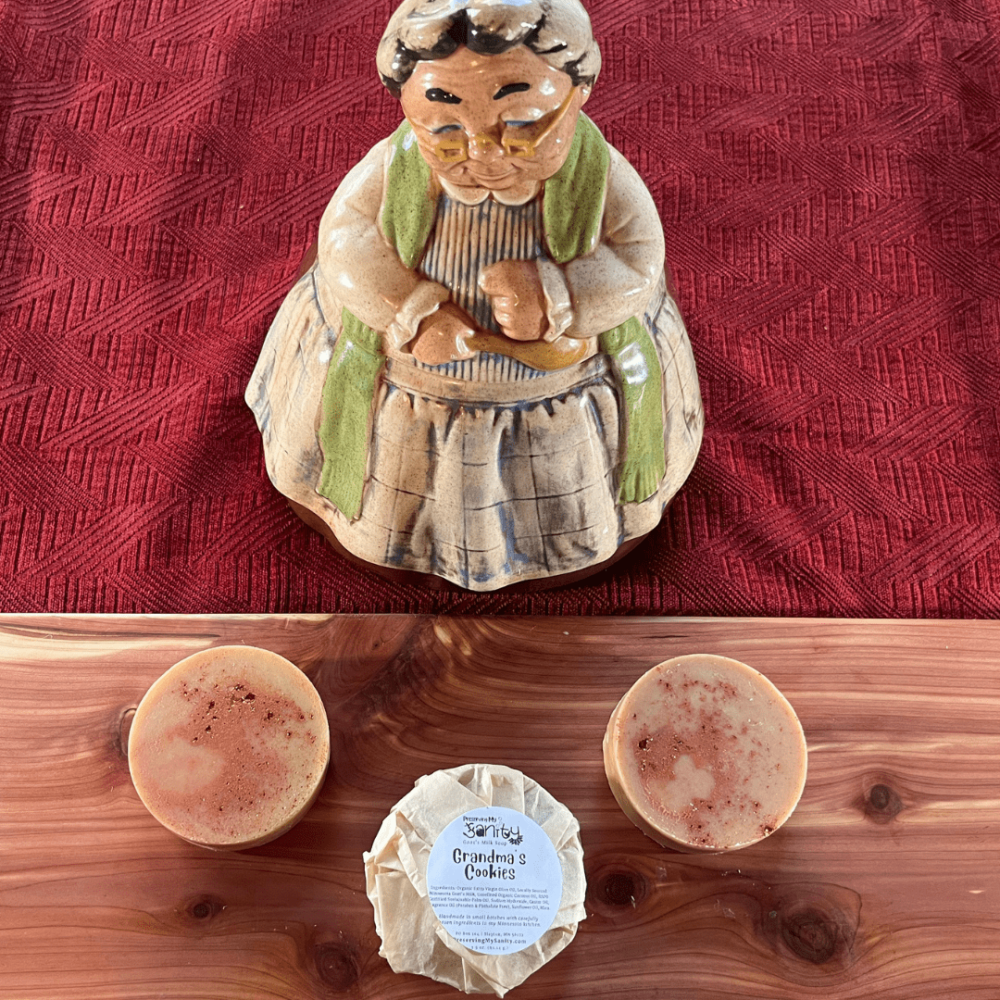 Three round bars of Grandma's Cookies soap on a cedar board, with a cookie jar of a baking grandma in the background