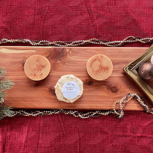 Holiday-themed flatlay featuring three round bars of Grandma's Cookies handcrafted goat's milk soap on a cedar board