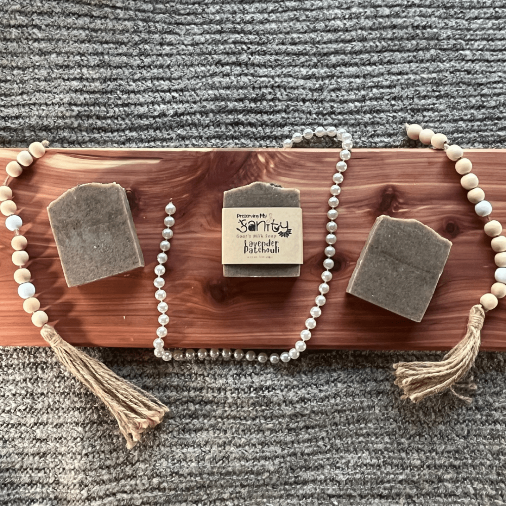 Pretty flatlay photo of three bars of Lavender Patchouli essential oil soap made with goat's milk on a cedar board with gray sweater backdrop