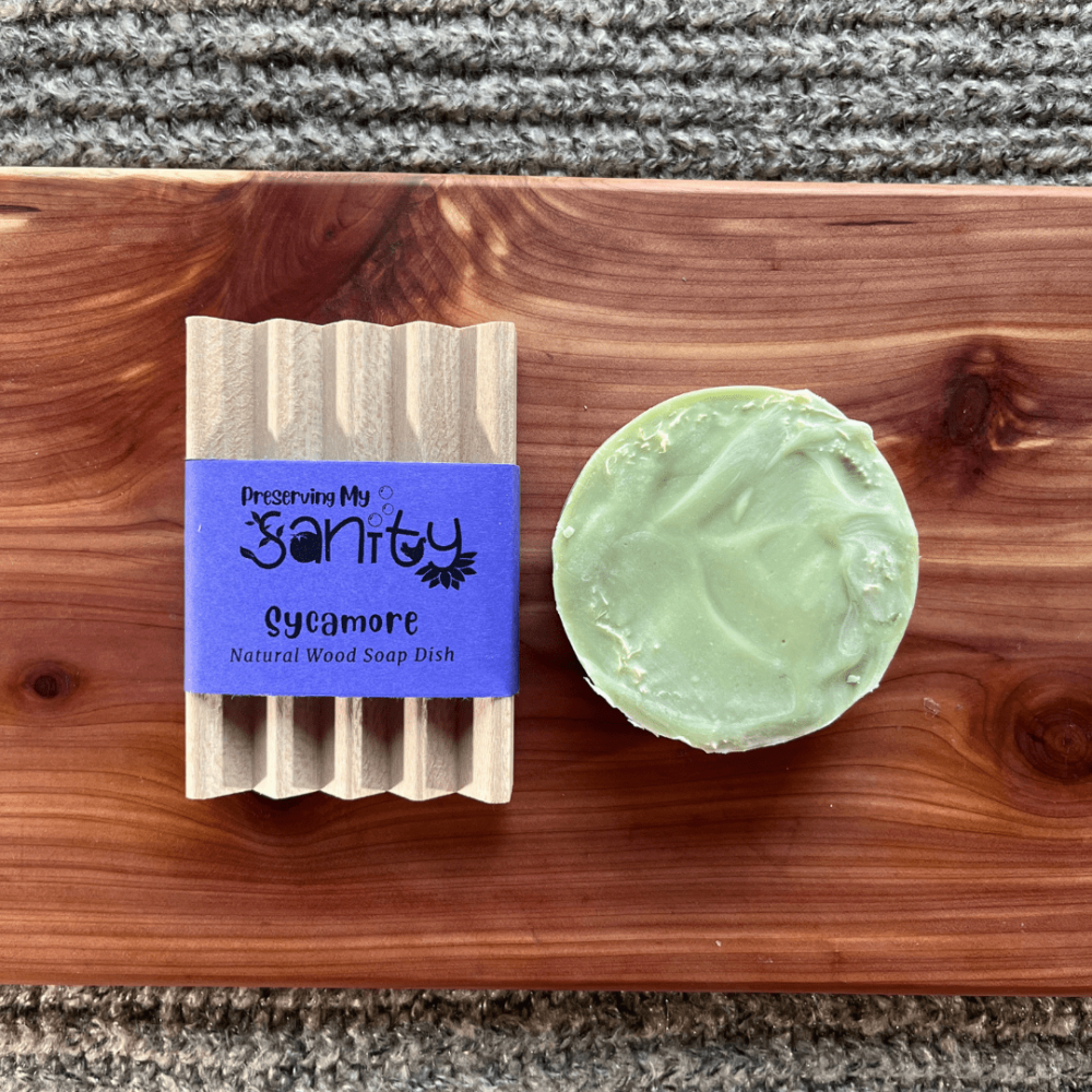 Flatlay photo of a Beachy Luffa/Loofah round bar of soap and a natural wood soap dish on a cedar board with a gray sweater backdrop
