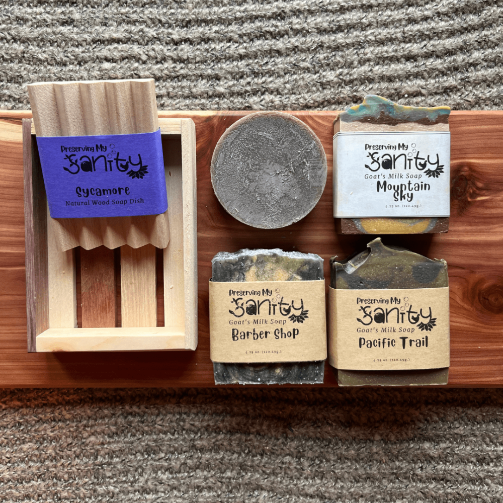 Flatlay photo of the masculine soap bundle that includes three bars of goat's milk soap, one bar of shaving soap, a wood soap dish, and a reclaimed wood gift tray