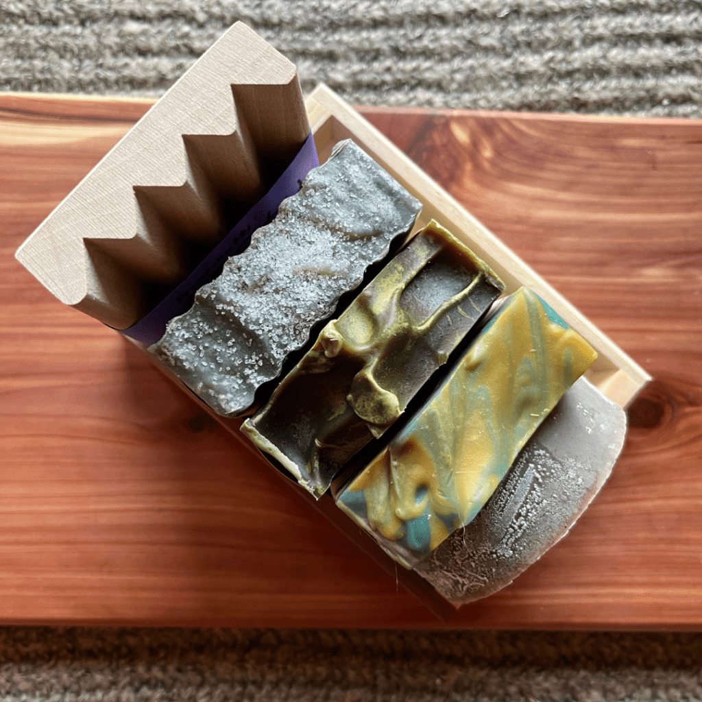 Overhead view of he masculine soap bundle that includes three bars of goat's milk soap, one bar of shaving soap, a wood soap dish, and a reclaimed wood gift tray
