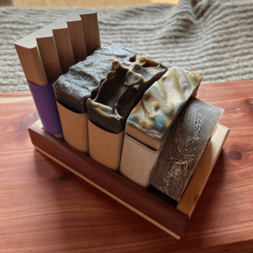 Side view of the masculine soap bundle that includes three bars of goat's milk soap, one bar of shaving soap, a wood soap dish, and a reclaimed wood gift tray