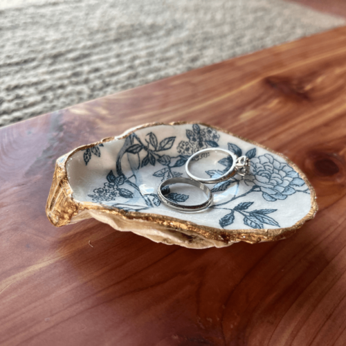 Alternate view of a handcrafted oyster shell ring dish with two rings in it, sitting on a pretty cedar board