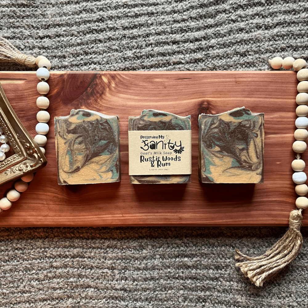 Flatlay photo of three bars of rustic woods and rum goat's milk soap on a cedar board