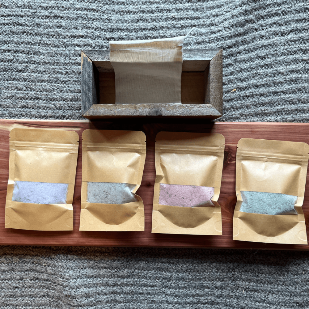 Flatlay photo of four kinds of bath salts on a cedar board, with a reusable cheesecloth bag and reclaimed wood trough for gifting
