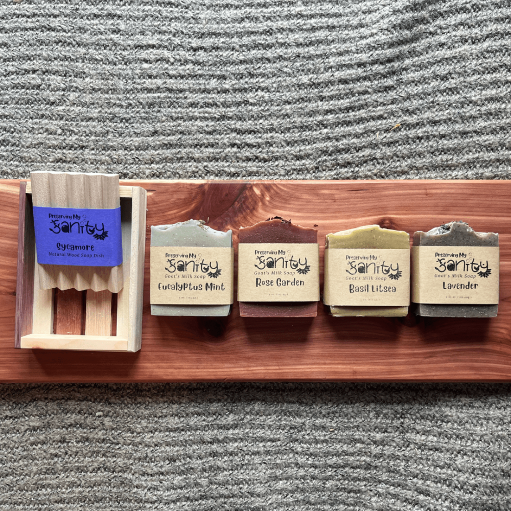 Flatlay photo of four bars of essential oil soap, a wood soap dish, and a reclaimed wood gift tray sitting on a cedar bath board