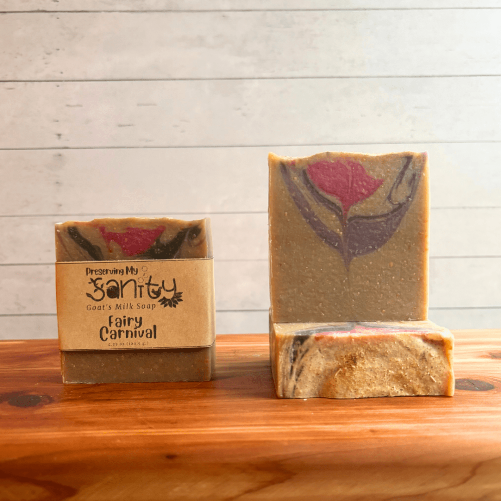 Three bars of Fairy Carnival goat milk soap with a white backdrop on a cedar board. Soap is a light beige color with a subtle swirl of purple, pink, and silver.