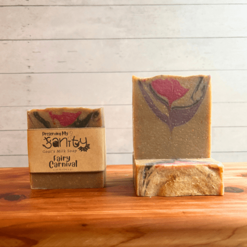 Three bars of Fairy Carnival goat milk soap with a white backdrop on a cedar board. Soap is a light beige color with a subtle swirl of purple, pink, and silver.