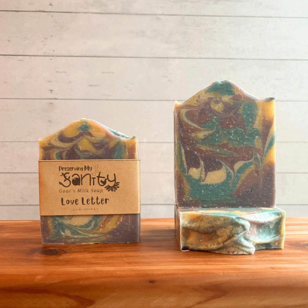 Three bars of Love Letter goat milk soap with a white backdrop on a cedar board. Soap is pastel colors inspired by conversation hearts that are swirled together in a pretty pattern.