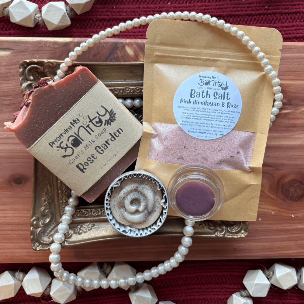 Flatlay photo of items included in Rose Garden bundle - a bar of goat's milk soap, a pouch of bath salt, a lotion bar, and a lip butter