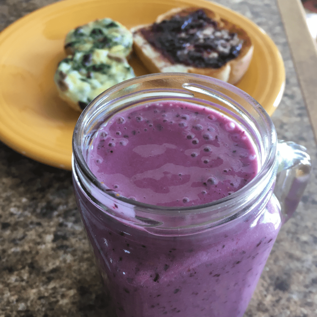 Photo of a purple fruit and vegetable smoothie with a plate of breakfast in the background