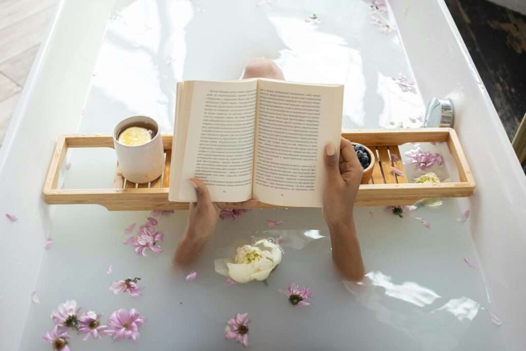 Overhead photo of a woman reading a book while sitting in a bath filled with pretty fresh flowers.