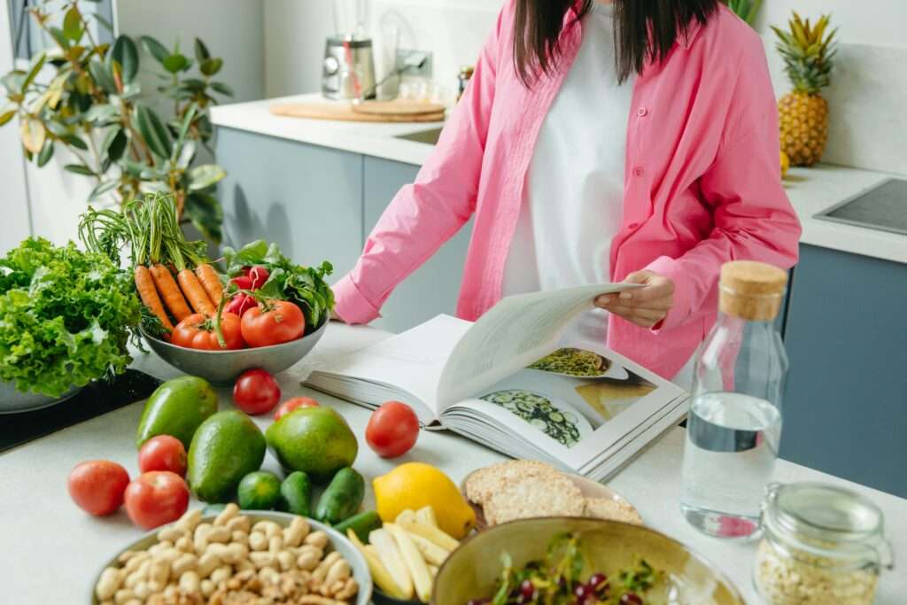 Photo of a woman in a bright kitchen who is paging through a cookbook while surrounded by fresh produce