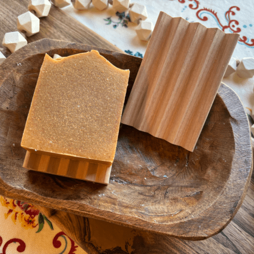Flatlay photo of two natural wood soap dishes, one featuring a handcrafted bar of goat's milk soap