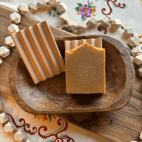 Flatlay photo of two natural wood soap dishes, one featuring a bar of handcrafted goat's milk soap