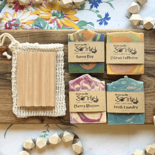 Flatlay view of items in spring soap sampler set on a natural finished board that includes four half-size bars of soap, a wood soap dish, and a soap saver bag