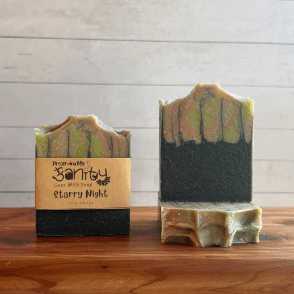 Three bars of Starry Night goat milk soap. Soap is a unique pattern of the bottom half being black with the top having swirls of green and pink to mimic the Northern Lights. Two bars are displayed to show the design and top of the bars, while the third shows the label.