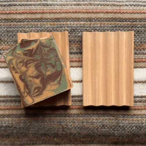 Photo of two natural wood soap dishes, one showcasing a bar of handcrafted goat's milk soap and the other plain to show craftsmanship