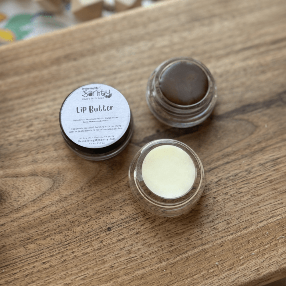 Flatlay photo of two small jars of lip butter - one plain/untinted and the other a plum brown/purple color.