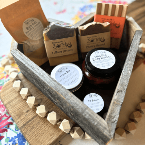 Additional photo of items included in the Mother's Day gift bundle - bath salt, lip butter, lotion bar, whipped body butter, two bars of goat's milk soap, and a natural wood soap dish. Items displayed in a handcrafted reclaimed wood heart box, which is for sale as an add-on to your purchase.