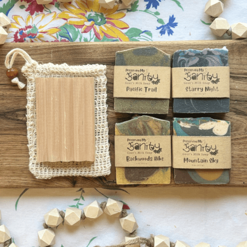 Overhead flatlay view of the masculine soap sampler, featuring four half-size bars of soap, a soap saver bag, and a natural wood soap dish - all sitting on a wood board