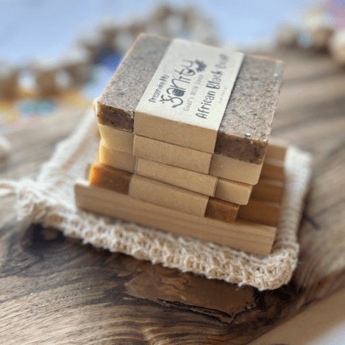 Flatlay side view photo of four half-size bars of unscented soap, a natural wood soap dish, and a natural fiber soap saver bag